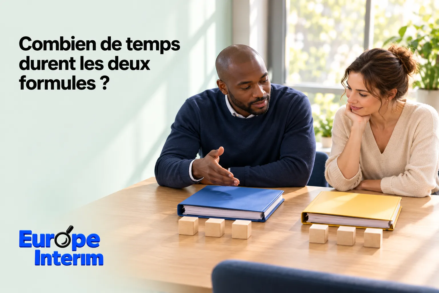 Deux personnes discutent assises à une table de bureau avec des dossiers et des blocs en bois devant elles.